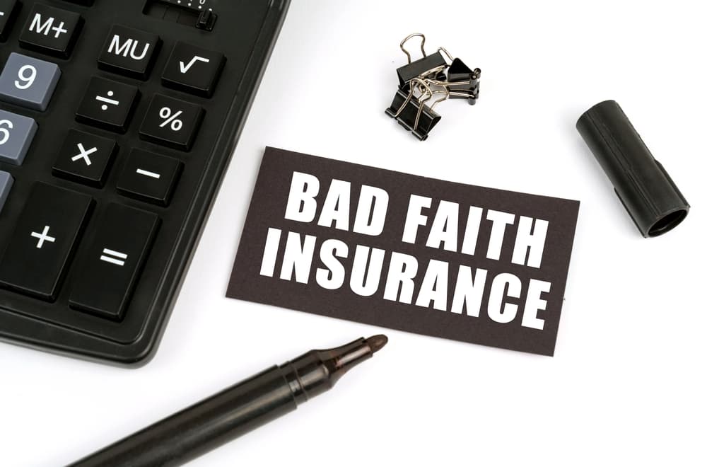 A business and finance concept featuring a white table that displays a calculator, a marker, and a black plate inscribed with "Bad Faith Insurance."






