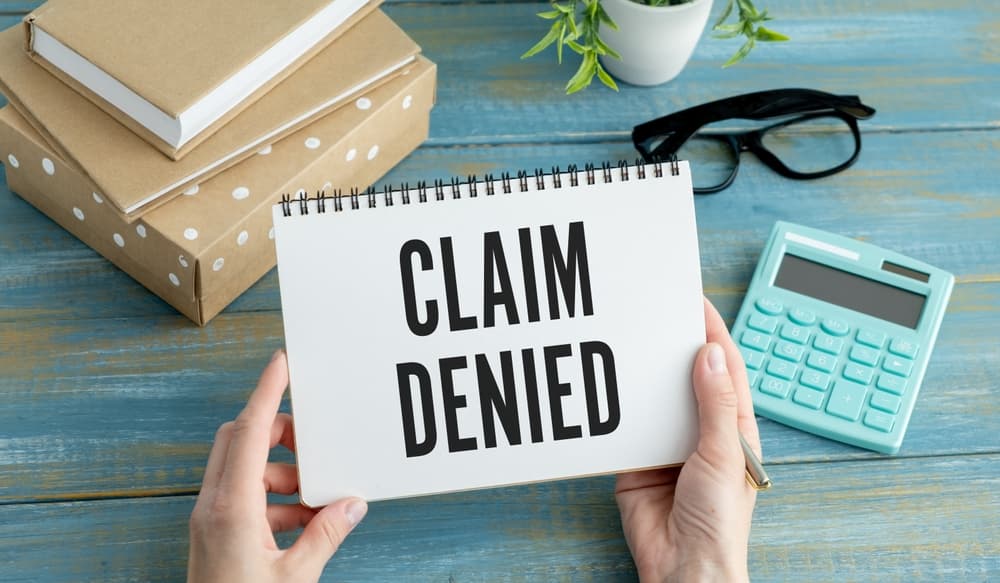 A businesswoman holds a card displaying the text "Claim Denied," symbolizing an injury claim insurance concept.






