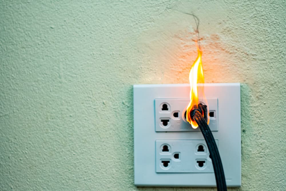 An electrical short circuit causes the wall receptacle to catch fire, resulting in burnt wires and damage to the partition.