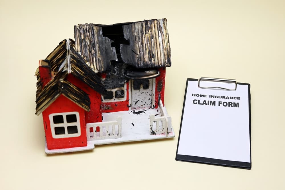 A home insurance claim form beside a model house showing fire damage.