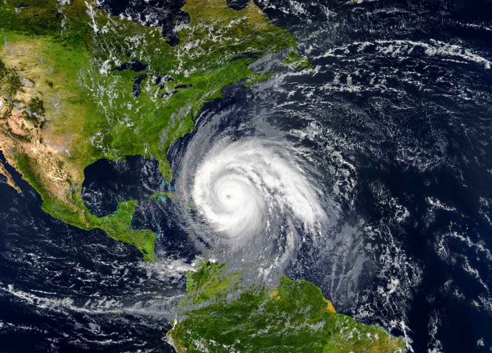 A massive tropical hurricane is closing in on the U.S. coastline, its swirling cloud bands spanning hundreds of miles. The satellite view shows a well-defined eye at the storm's center, encircled by dense, spiraling clouds as it gains intensity over the ocean.