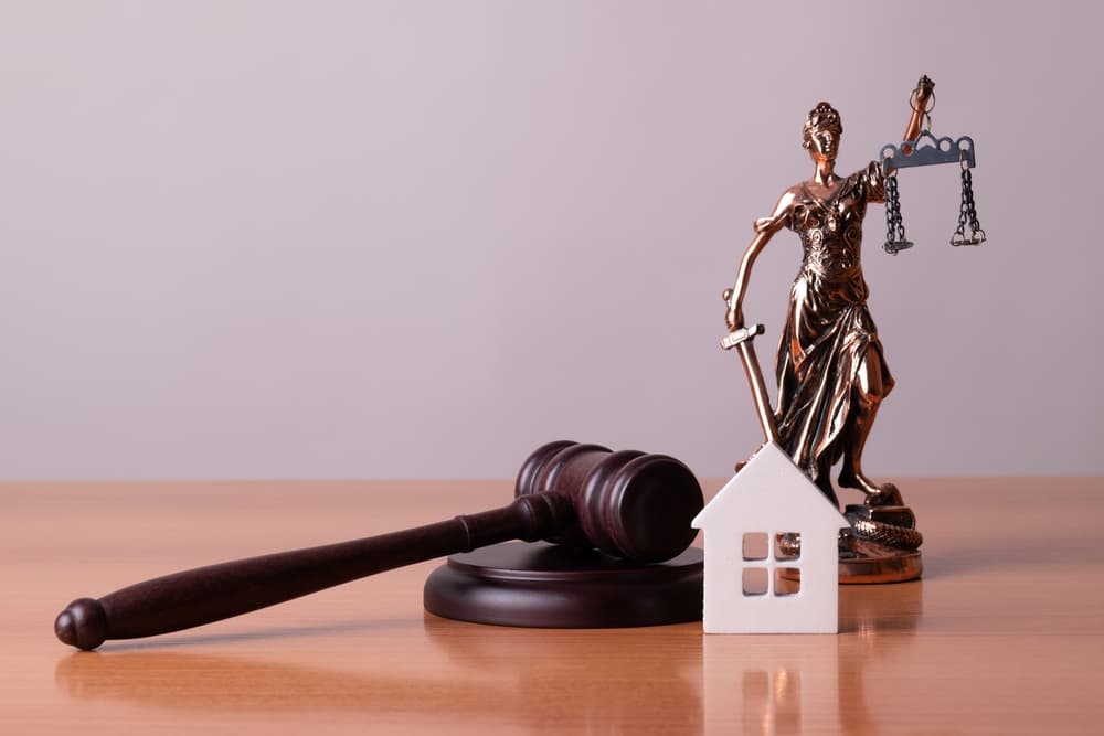 Lady Justice stands prominently alongside a judge's gavel and a house, symbolizing the legal concepts of real estate auctions, property division during divorce, and the law's role in managing asset distribution.