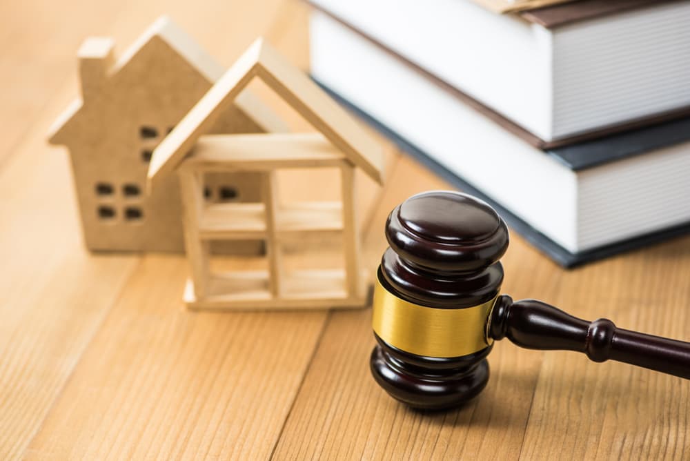 A gavel rests on a wooden table, with a wooden house in the background, symbolizing justice and legal matters.