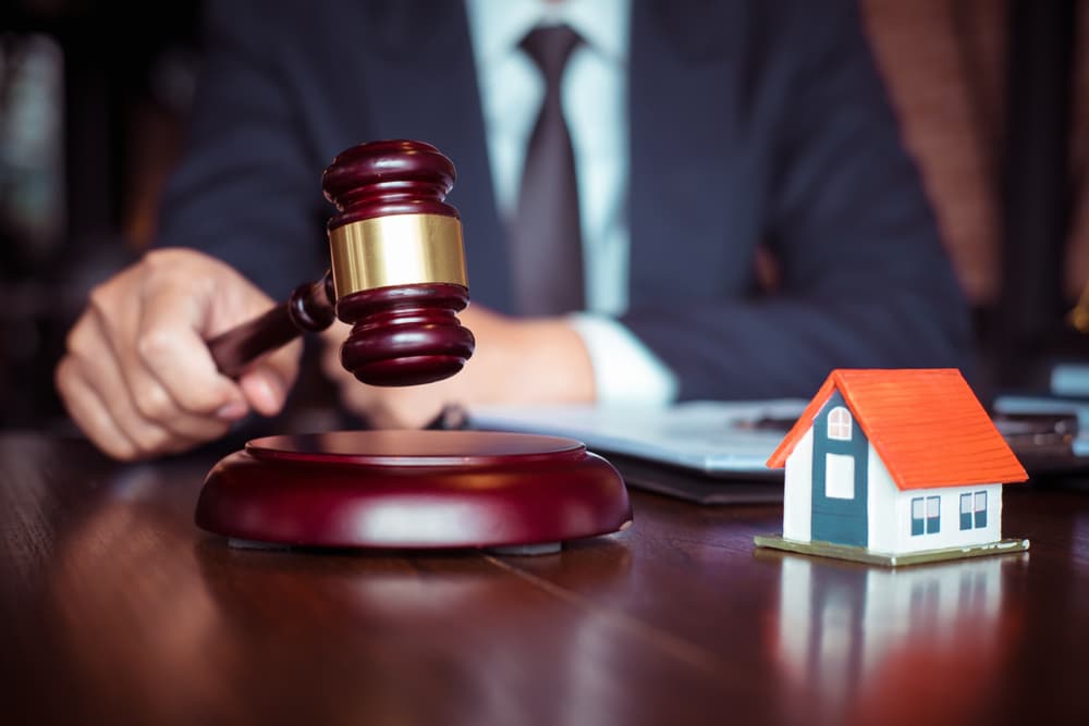 The concept of justice and law is depicted with a judge's gavel resting on a sounding block. A male judge holds it in the courtroom while reviewing case documents and law books at the table.