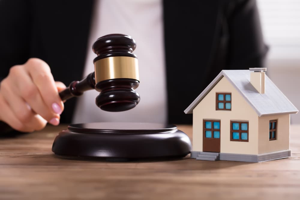 Close-up of a judge’s hand striking a gavel near a house model on a desk.






