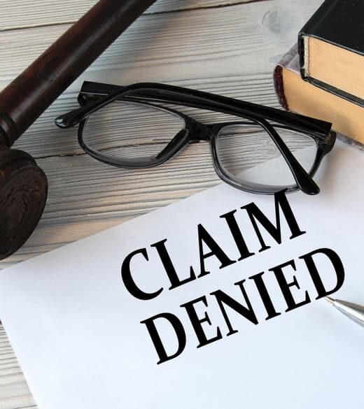 "CLAIM DENIED" written on white paper, set against a background featuring a judge's gavel, eyeglasses, and a pen.