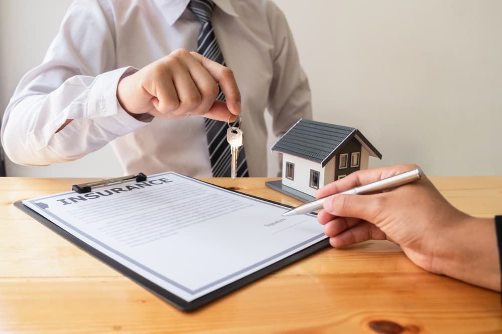 An agent hands a key to a customer after providing guidance on selecting house insurance, symbolizing completion of the insurance process. This captures the finance and insurance concept of securing a home.