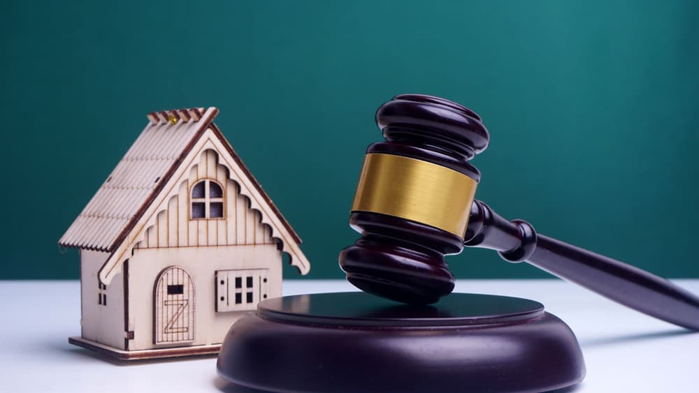 A judge's gavel beside a house model on a green background, symbolizing real estate and financial decisions.